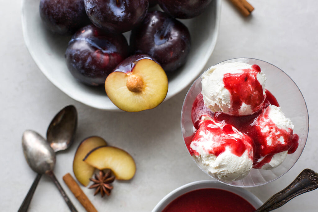 overhead image of spiced plum sauce over vanilla ice cream in bowl with second bowl of plums next to it